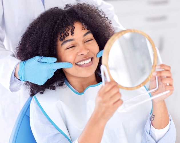 Woman smiling in front of mirror after dental cleaning and exam in Waco